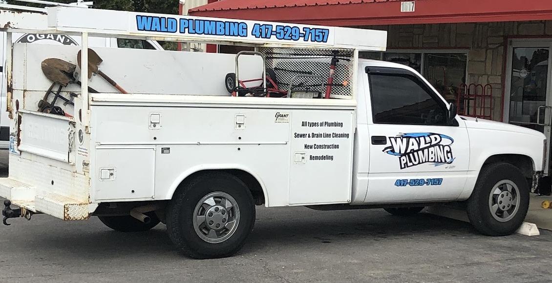 The Wald Plumbing service truck, a white utility bed pickup with the wordmark on the door and the service list on the bed